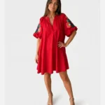 Femme portant une robe courte rouge fluide à encolure fendue et manches ballon ornées de broderies florales multicolores.