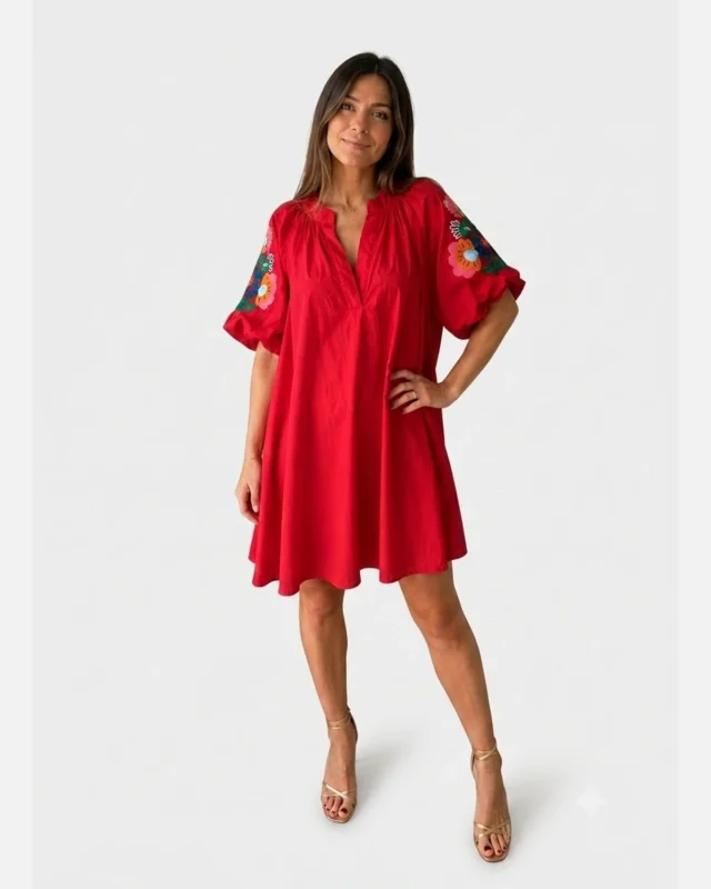 Femme portant une robe courte rouge fluide à encolure fendue et manches ballon ornées de broderies florales multicolores.