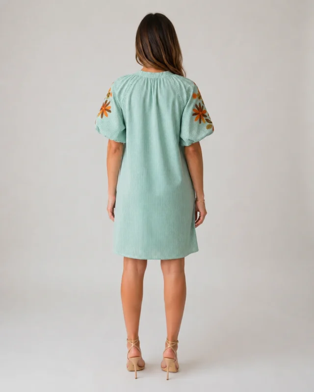 Femme portant de dos une robe courte vert d’eau à fines rayures verticales et broderies florales sur les manches